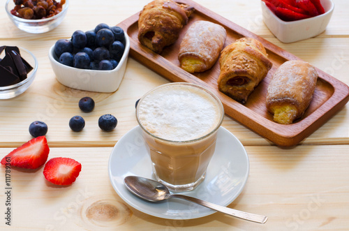 Beautiful  breakfast. Glass cup of coffee with milk served with crushed chocolate, different pastries, berries and raisins on the wooden background.