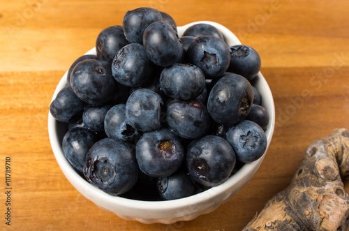 Blueberries in a white bowl on a wooden cutting board.