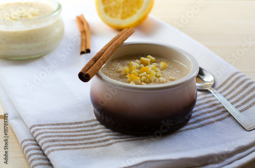 Homemade rice pudding in a ceramic bowl with sticks of cinnamon and lemon on wooden background. Delicious healthy dessert.