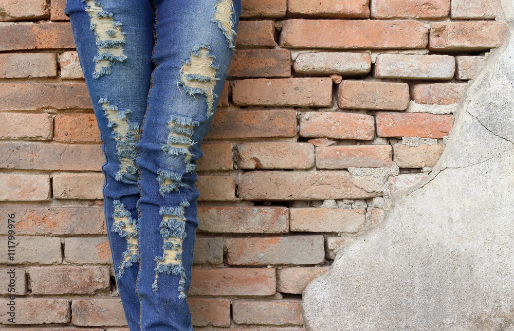 Female legs in fashionable jeans stands in brick block wall