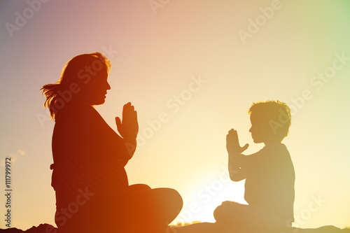 Silhouette of pregnant mother and son doing yoga on beach