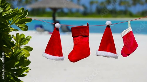 Red Santa hats and Christmas stocking hanging on tropical beach