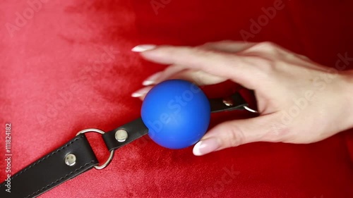 Fetish bdsm gag in female hand. sex toys. red sheets