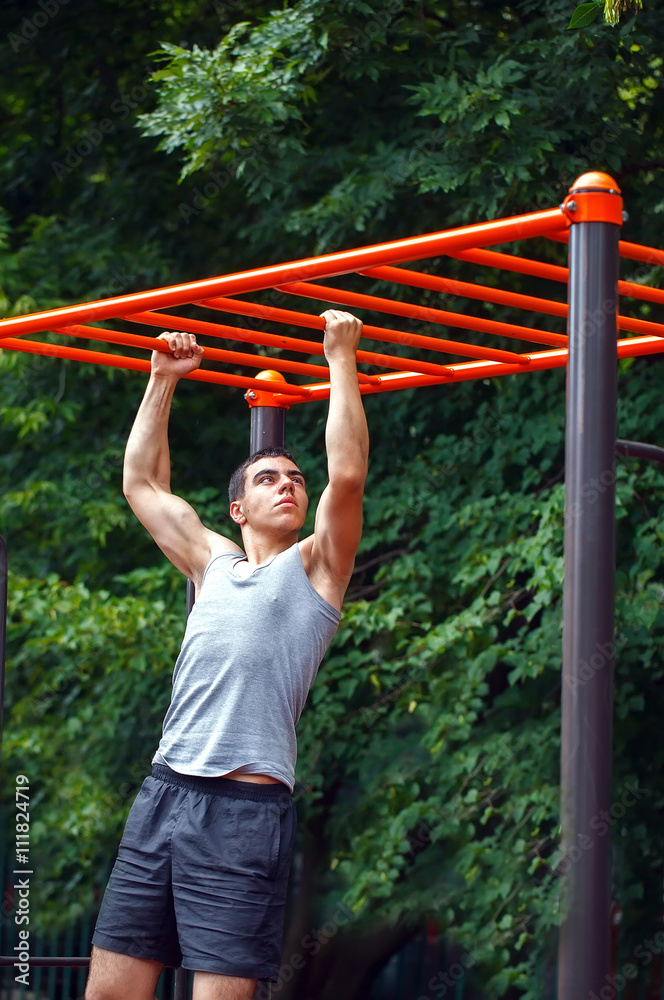 Fototapeta premium Muscular man doing pull-ups on horizontal bar