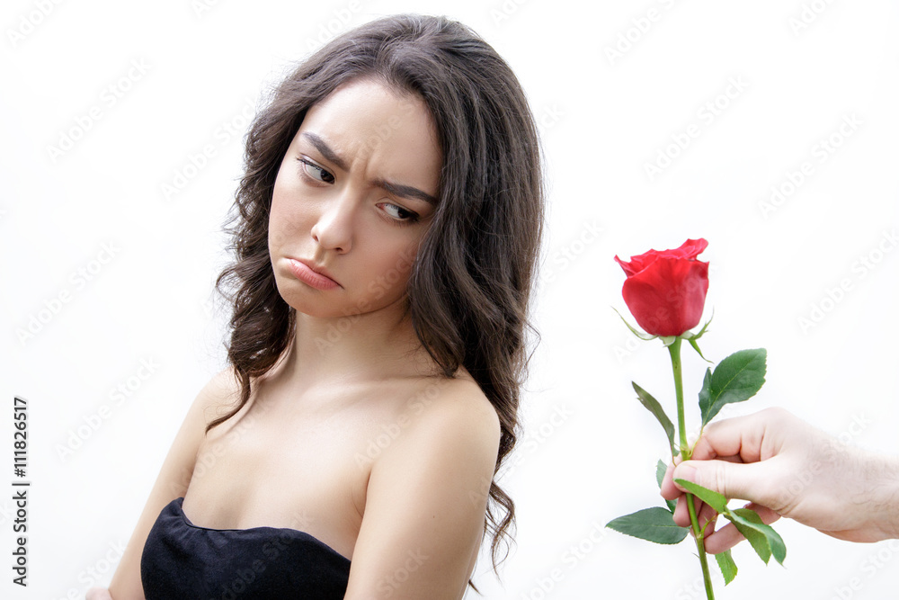 Beautiful upset girl receives one red rose. She is looking over her shoulder and pouts. Men's hand holding one rose. Girl is white with bushy brown hair. Isolated on white background. Beautiful upset girl receives one red rose. She is looking over her shoulder and pouts. Men's hand holding one rose. Girl is white with bushy brown hair. Isolated on white background.