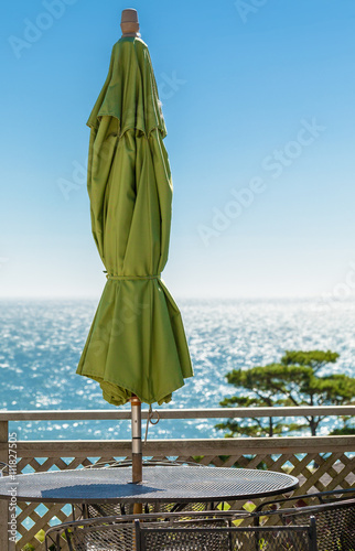 Outdoor deck table with sun umbrella overlooking sparkling sea © Crin