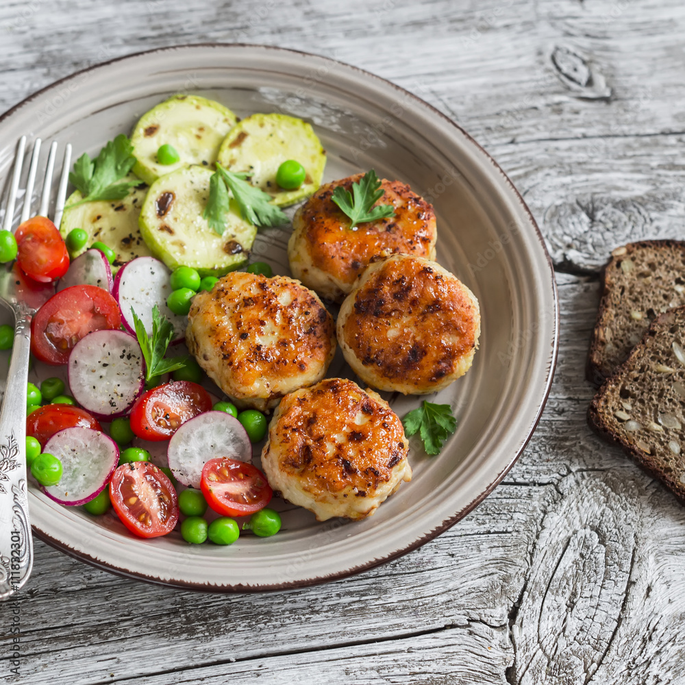 Chicken cutlets, grilled zucchini and fresh vegetable salad on rustic light wood background