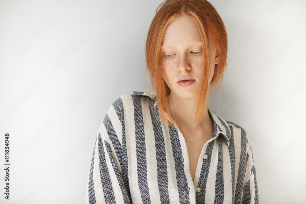 People and lifestyle concept. Close up shot of female student wearing striped pajamas at home in the morning before going to school. Pretty teenage girl with freckles and ginger hair looking down People and lifestyle concept. Close up shot of female student wearing striped pajamas at home in the morning before going to school. Pretty teenage girl with freckles and ginger hair looking down