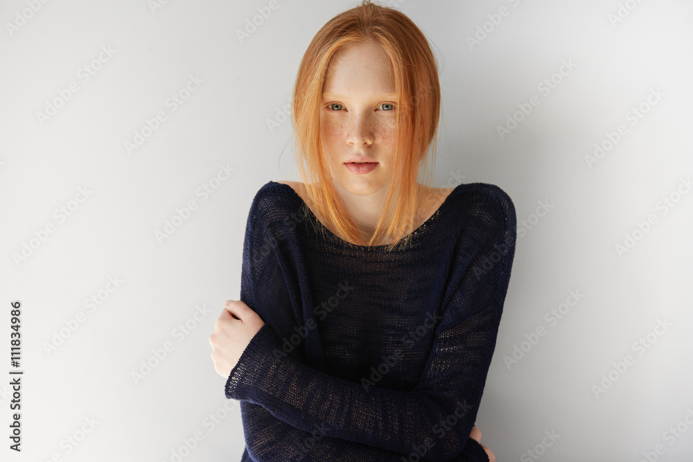 Close up portrait of sad or disappointed young woman with red hair wearing casual top, looking at the camera with unhappy expression, holding arms folded. Human face expressions and emotions Close up portrait of sad or disappointed young woman with red hair wearing casual top, looking at the camera with unhappy expression, holding arms folded. Human face expressions and emotions
