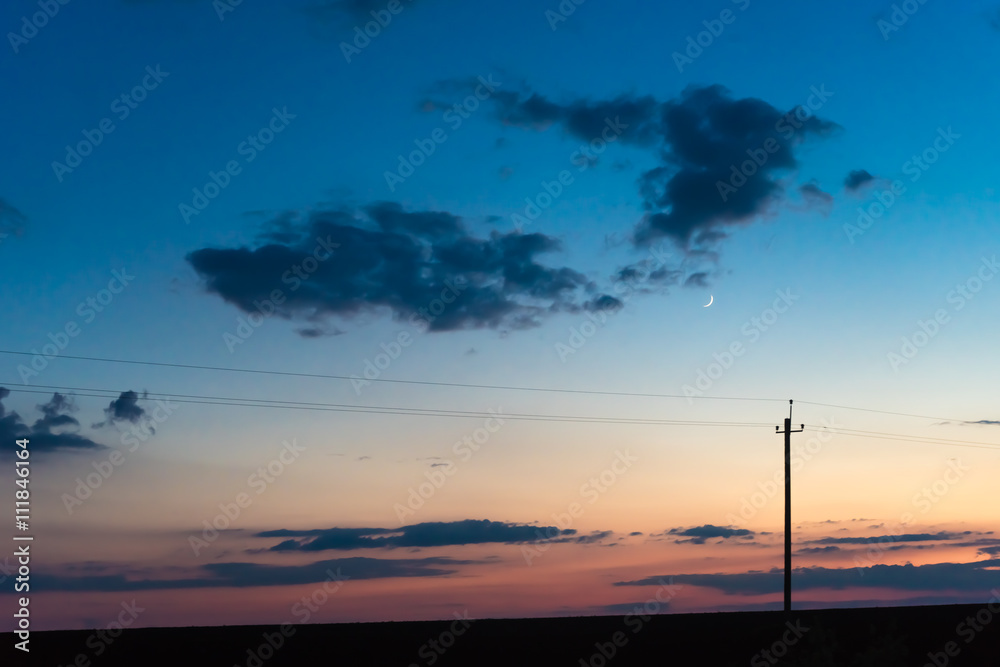 electric pole on the background of sunset sky with clouds and moon