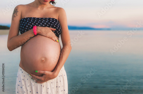 Young happy pregnant woman at the beach at sunset