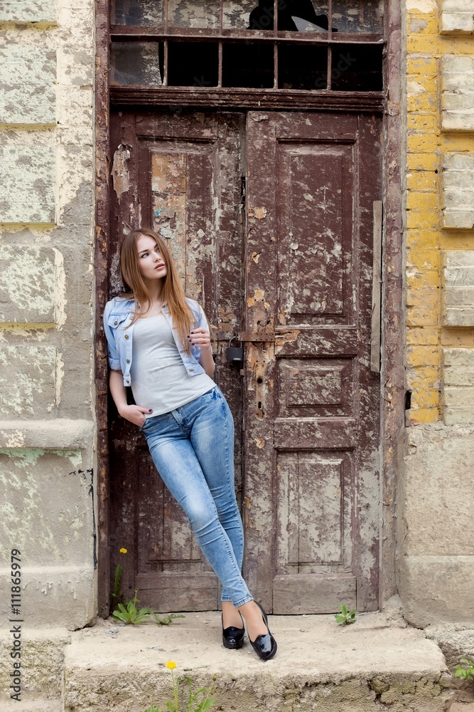 beautiful young sweet girl with red hair in jeans standing near the door of the old city beautiful young sweet girl with red hair in jeans standing near the door of the old city