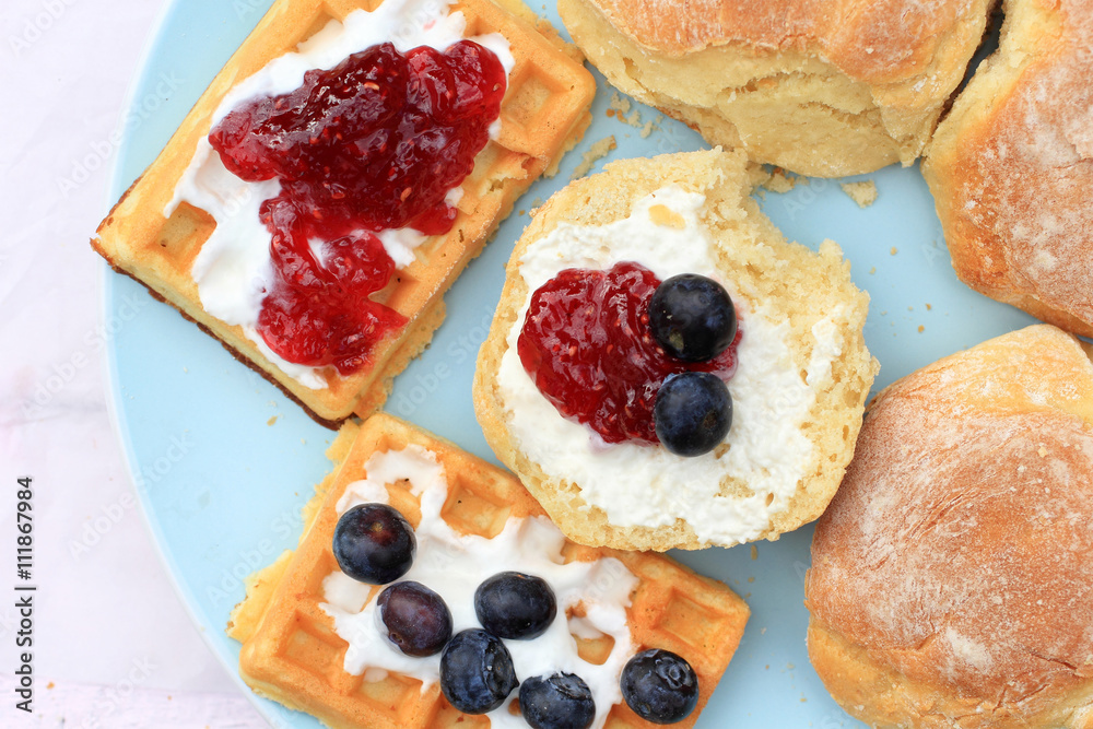 Fresh Scottish scones and belgian waffles with cream and raspberry jam and blueberries Fresh Scottish scones and belgian waffles with cream and raspberry jam and blueberries