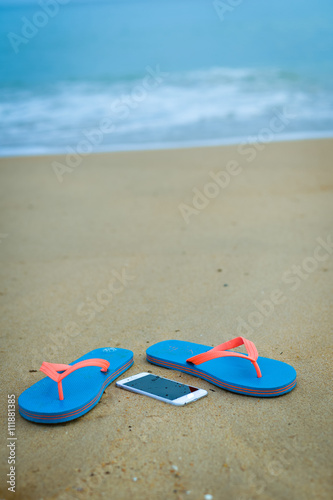 Top view close up on mobile phone with slippers on summer beach background. Happy joyful vacation