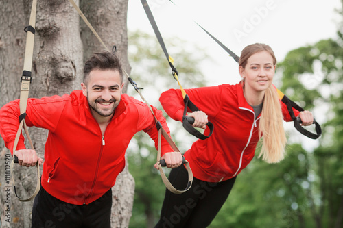 Happy sport man and woman training in park with suspension trainer sling preparing for jogging long distances.