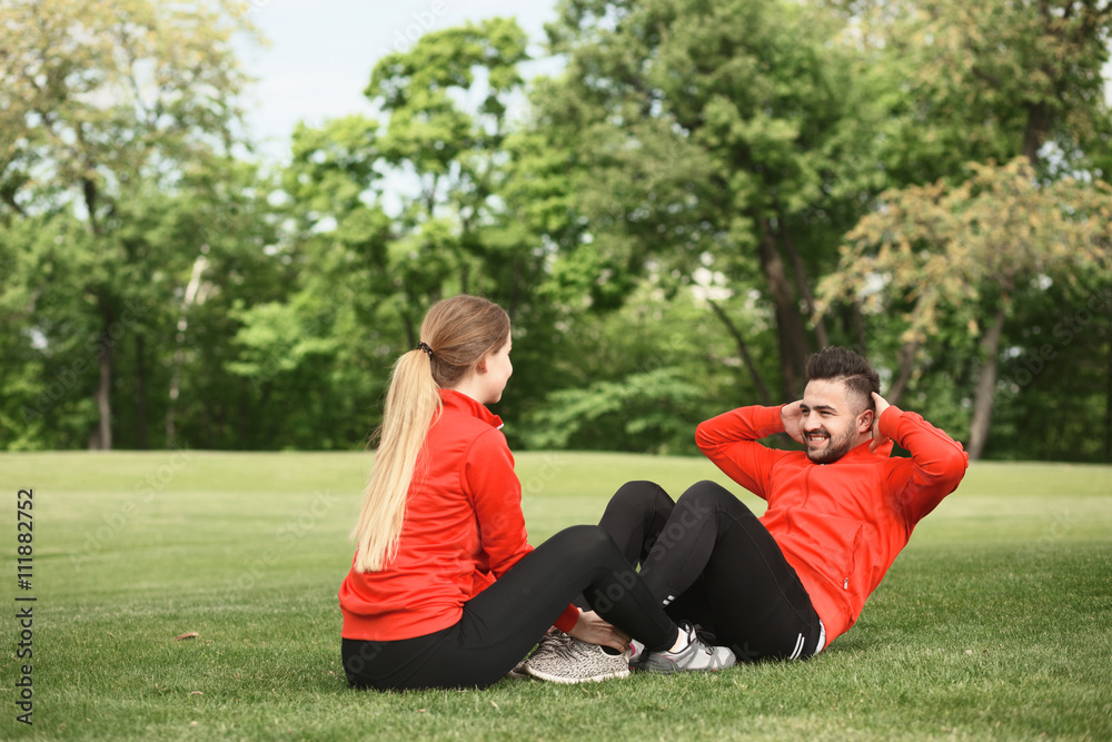 Sport man training in park doing abdominal crunches. Group of man and woman exercising on fresh air in green park or forest.