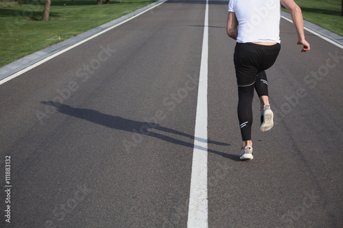 Jogging man along road. Closeup of male in running shoes going for run on road at sunrise or sunset. Fitness or sport concept.