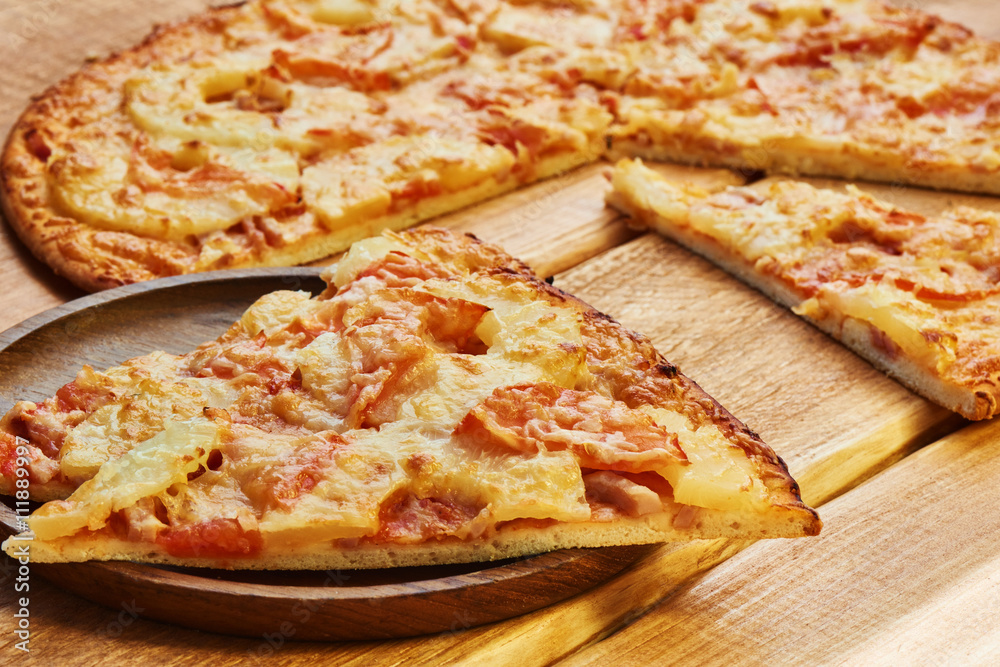 A slice of pizza with toppings of pineapple on a wooden plate A slice of pizza with toppings of pineapple on a wooden plate