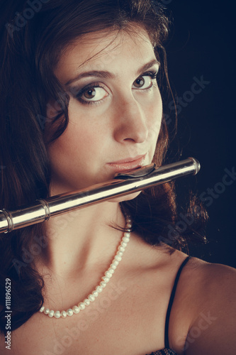 Woman playing transverse flute on black.