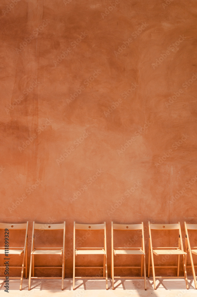 empty wooden chairs against orange cement wall empty wooden chairs against orange cement wall