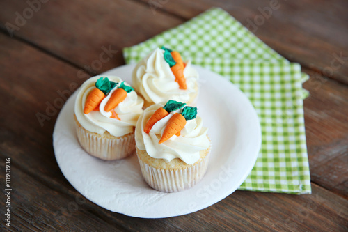 Cupcakes with frosting and decorative carrots on wooden background