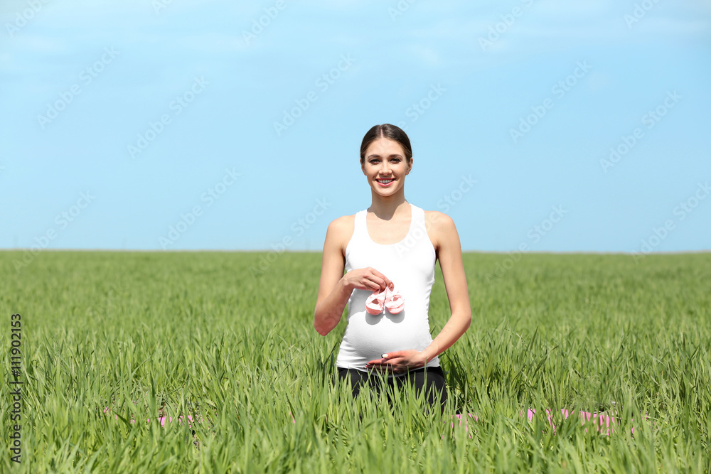 Pregnant woman holding baby's bootees in field Pregnant woman holding baby's bootees in field
