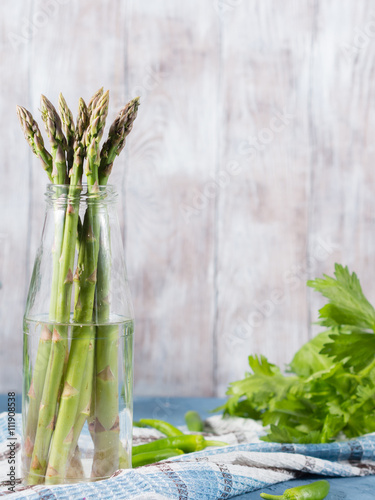 Organic asparagus in a glass bottle on napkin on wooden textured background. Vertical image  copy space