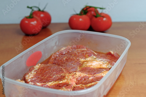 Raw marinated meat on a grill in a plastic bowl on wooden table, party