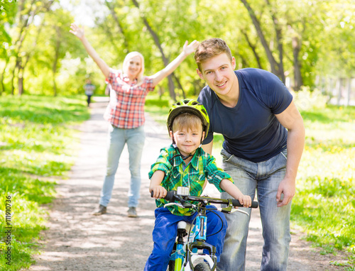 mum and dad taught his son to ride a bicycle in the park © Ermolaev Alexandr