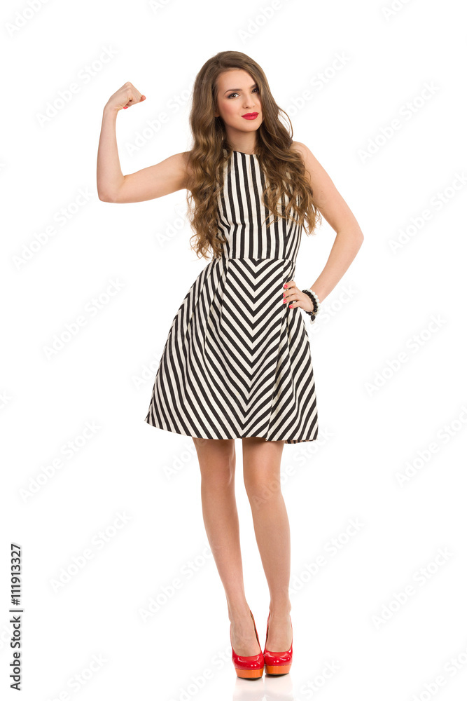 Cheerful attractive woman in black and white striped dress and high heels flexing biceps Cheerful attractive woman in black and white striped dress and high heels flexing biceps