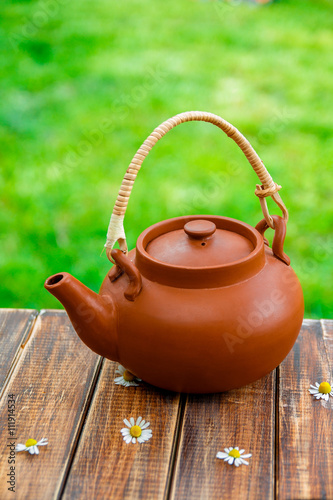 Brown teapot on wooden with chamomile table in garden and on nature background. Closeup. Tea concept. Closeup