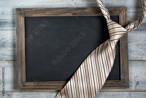 Fathers day concept, empty framed chalkboard and tie on wooden background
