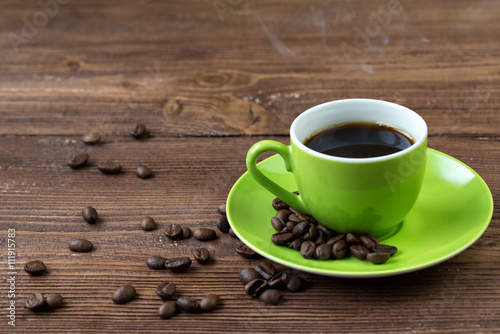 Green cup of hot coffee and coffee beans on wooden table