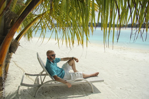  bald  man on a sun lounger under a palm tree in the Maldivian b © vrangel
