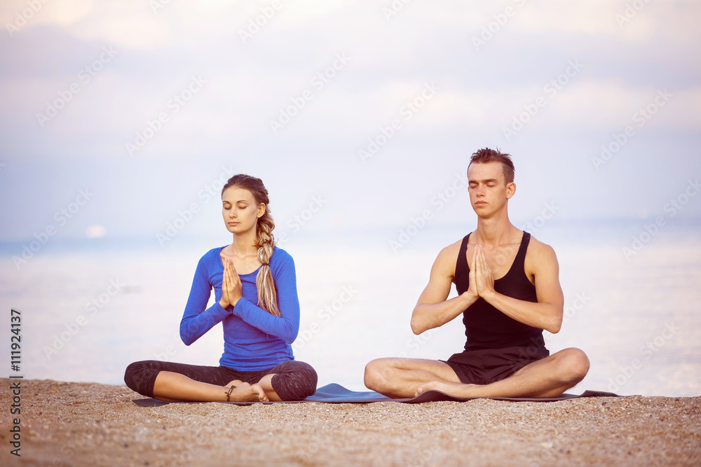 Young couple is practicing yoga at golden sea sunrise background Young couple is practicing yoga at golden sea sunrise background