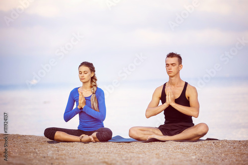 Young couple is practicing yoga at golden sea sunrise background