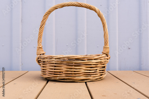 Long handled wicker basket on brown decking against rustic lilac external wall