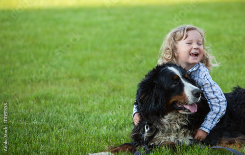 cute boy with curly blonde hair embraces a bernese mountain dog
 photo