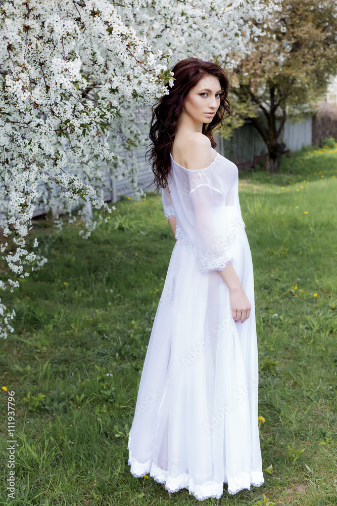 beautiful sexy cute gentle girl walks in a light white dress on a blossoming garden of bright summer day