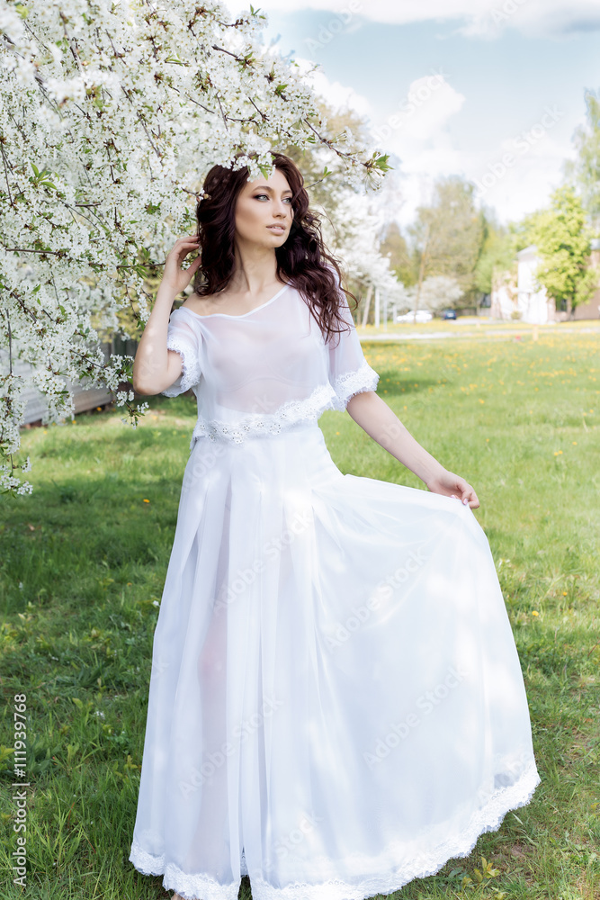 beautiful sexy cute gentle girl walks in a light white dress on a blossoming garden of bright summer day