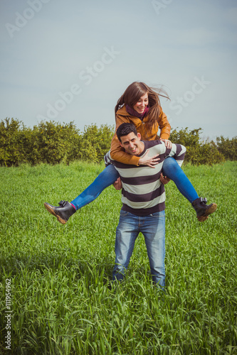 Young couple having fun together in green field. The woman ridin photo