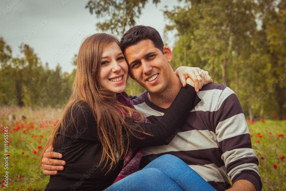 Young couple sitting on the grass in a field of red poppies and Young couple sitting on the grass in a field of red poppies and