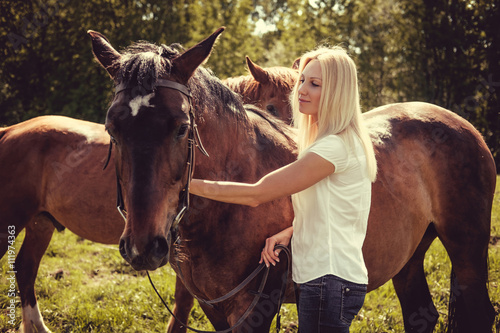 Blond female posing with brown horses in a field. © Fxquadro