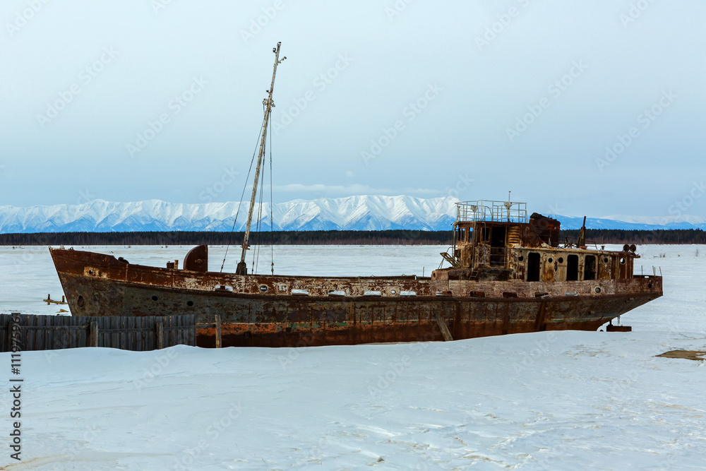 Old rusty ship on winter shore of Lake Baikal.