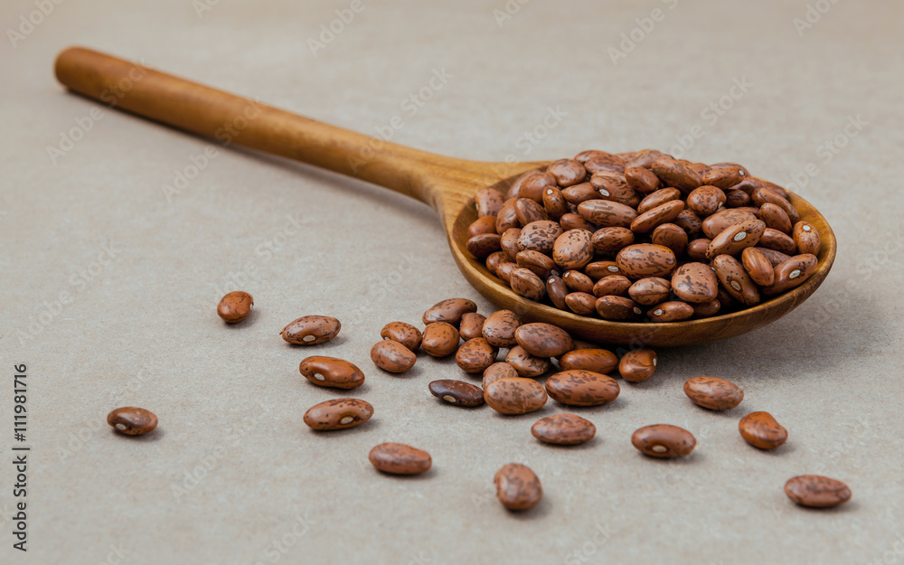 Obraz premium The composition of raw pinto beans in wooden spoon on brown back