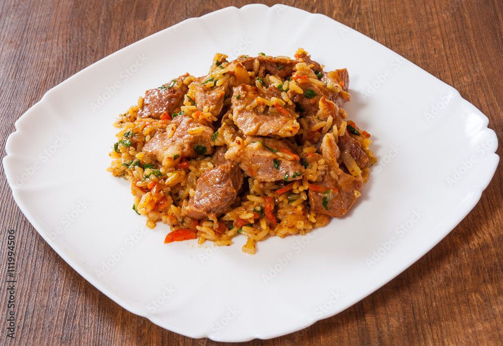 Rice with meat and vegetables in a plate on wooden table