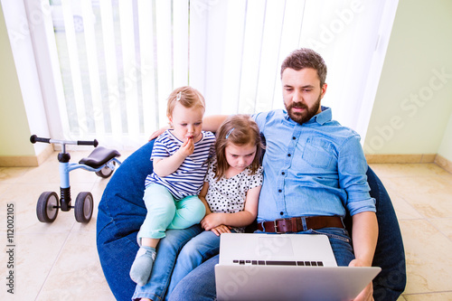 Father and daughters, playing on laptop, sitting on beanbag photo