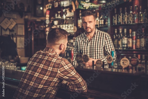 Tableau sur toile Handsome bartender pouring a pint of beer to customer in a pub.