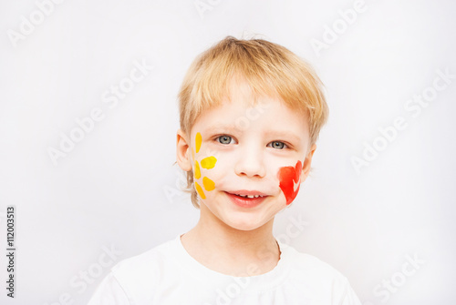 Beautiful smiling child face. Portrait of laughing emotional kid. Close up of cheerful funny boy isolated on white background. Baby with red heart and yellow sun on cheeks. Positive human emotions.