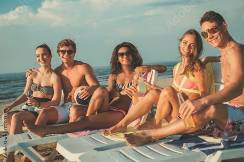 Quadro em tela Group of multi ethnic friends sunbathing on a deck chairs on a beach